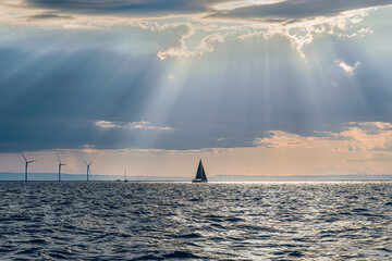 Apulian seascape: Gulf of Taranto. A sailboat on the horizon and wind turbines illuminated by the...