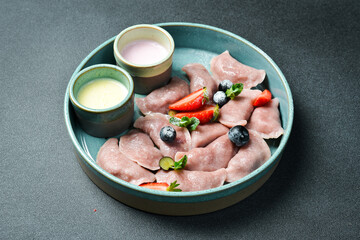 Dumplings with strawberries and sour cream. On a black stone background. In a plate, close-up.