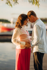 man and pregnant woman in red dress at sunset on the pier 