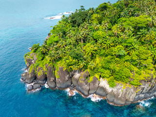 Steep rocky coastline of São Tomé covered in dense tropical vegetation and surrounded by vibrant...