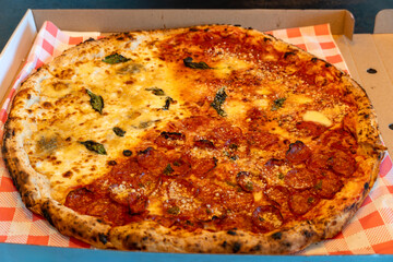 Overhead view of a freshly baked half cheese and half pepperoni pizza in a cardboard delivery box, with melted cheese and basil leaves.