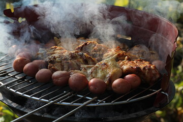 Grilling potatoes and chicken on an open flame, sizzling and golden-brown.