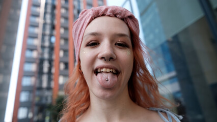 A teenage girl poses for a selfie on her smartphone. She shows her pierced tongue to her friends