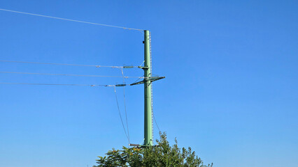 Detailed green power pole supports electrical cables above treetops with crisp blue background,...