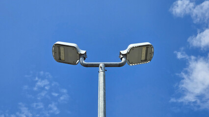 Pair of modern led lamps on galvanized metal pole stand tall, silhouetted against bright blue sky...