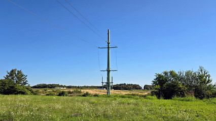 Tall green electricity transmission pole stands in an open countryside meadow filled with...