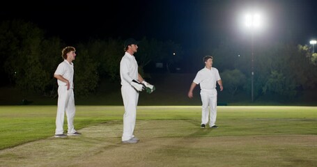 Three male cricketers catching and diving after ball being tossed under lights on pitch in practice - Powered by Adobe