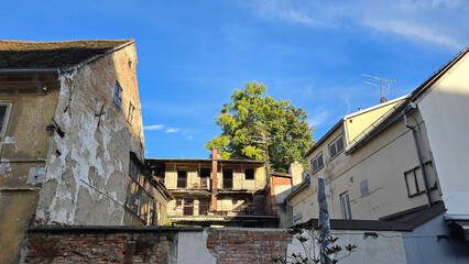 Old residential buildings with peeling plaster, exposed brickwork, and iron balconies face a green...