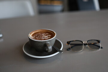 Close-up of a steaming cappuccino in a white ceramic mug, latte art heart design on frothy surface, warm café atmosphere.
