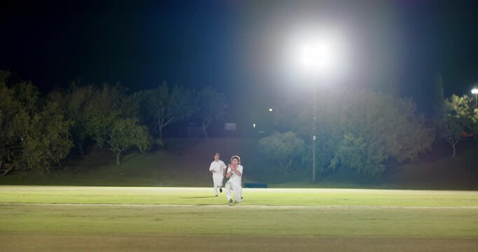 Running for bowled ball male fielder diving and snatching ball, teammates joining under floodlights