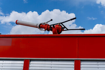 Water cannon on the roof of a red fire truck, aimed to the side, background with blue sky and white...