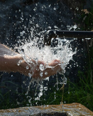 Fototapeta premium Quellwasser aus einem Brunnen spritzt auf Hände