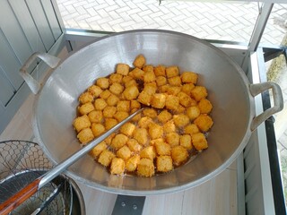 Tahu crispy or Golden crispy tofu cubes are being deep-fried in a large pan filled with hot oil, showing a delicious street food snack with crunchy texture and appetizing golden color.