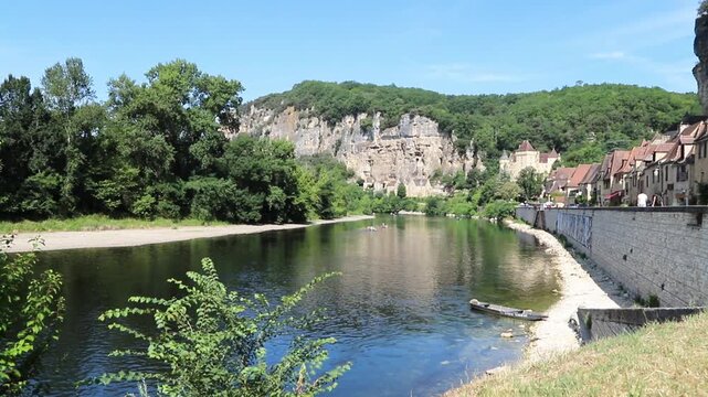 Scenic view in the village La Roque Gageac by the Dordogne River, backed by a steep cliff, Malartrie Castle in the background. showcasing lush greenery, tranquil waters, and charming architecture