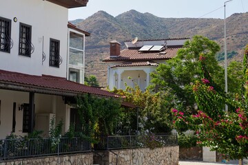 A building complex sits in front of a scenic mountain range, partially obscured by lush greenery in...