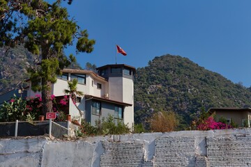 A modern house sits nestled against a mountain backdrop under a clear blue sky in Icmeler -...