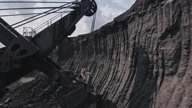 Work of big excavator removes overburden soil at open pit mine, FPV drone view of mining industry.