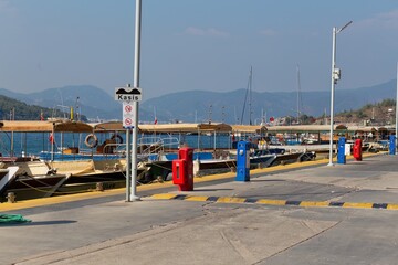 A harbor scene with a pole, two colorful bins, and boats in the background in Icmeler - Marmaris -...