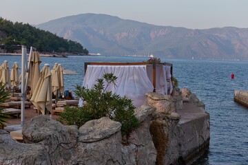 Beach umbrellas and lounge chairs line the shore, with mountains visible across the water in...