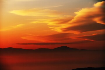 Stunning sunset paints sky with vibrant orange and golden clouds over silhouetted mountain range