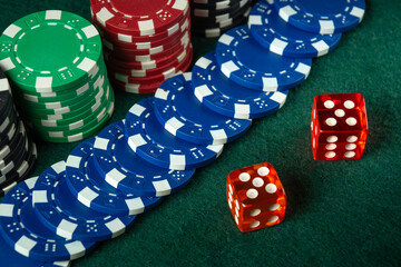 Colorful casino chips in red, green, and blue are arranged next to two red dice on a green felt...