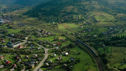 Aerial drone footage of a train moving through scenic mountains near a small settlement. Concept of...