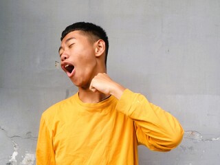 An Asian Indonesian boy in a yellow shirt expresses a mix of frustration and humor with a...