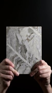 Luxury quartz stone texture pattern with trendy curly veins. Marble slab in hand on black background in Slow motion