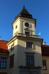 Fototapeta premium Clock tower of Tarnowski Castle in Tarnobrzeg, Poland, photographed in 2024, with bright facade, red roof and clear blue summer sky.