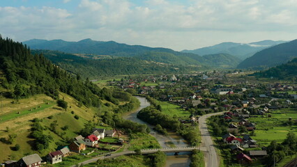 Aerial drone footage of a train moving through scenic mountains near a small settlement. Concept of...