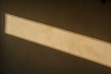 Warm golden sunlight casts a diagonal beam across a textured beige wall, creating a serene and modern ambiance for backgrounds.