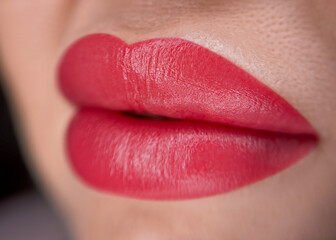 Close-up of full lips with bright red lipstick. The skin is smooth and well-groomed, highlighting...