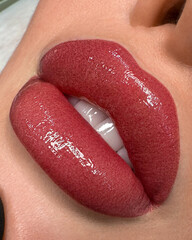 Close-up of glossy, full lips with a rich red lipstick shade. The lips are well-defined and...