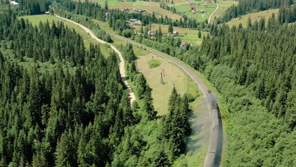 Aerial drone footage of a train moving through scenic mountains near a small settlement. Concept of...