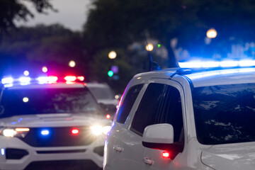 Police units respond to the scene of an emergency with illuminated red and blue lights at dusk.