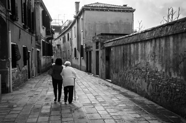 Una donna anziana cammina sotto braccio alla figlia in una calle di Venezia