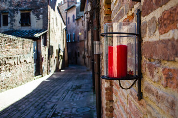 Una candela rossa in una lanterna di vetro appesa a un muro lungo una strada del borgo di Certaldo...