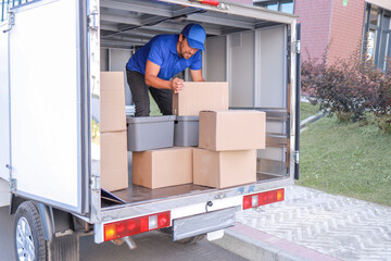 an employee in a blue uniform loads a truck with boxes for transportation. concept logistics, small...