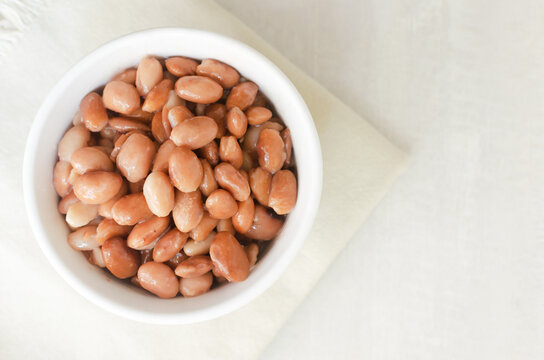 Boiled borlotti beans in a white bowl on a napkin on a gray background. Italian cuisine. Vegan and vegetarian food. Selective focus. Horizontal orientation. Copy space. Top view