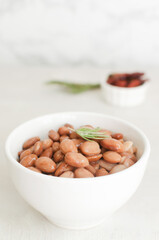 Boiled borlotti beans in a white bowl with a sprig of rosemary and sun-dried tomatoes on a gray...