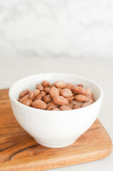 Boiled borlotti beans in a white bowl on a wooden cutting board on a gray background. Italian cuisine. Vegan and vegetarian food. Selective focus. Vertical orientation.