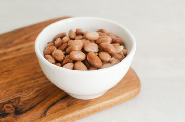 Boiled borlotti beans in a white bowl on a wooden cutting board on a gray background. Italian...