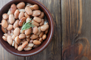 Boiled borlotti beans in a brown bowl with rosemary on a wooden background. Italian cuisine. Vegan and vegetarian food. Selective focus. Horizontal orientation. Top view. Copy space