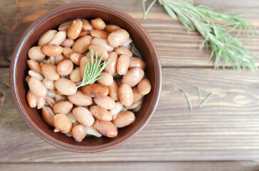 Boiled borlotti beans in a brown bowl with rosemary on a wooden background. Italian cuisine. Vegan and vegetarian food. Selective focus. Horizontal orientation. Top view. Copy space