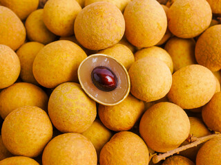 Fresh longan fruits with light brown skin, one opened to reveal the translucent flesh and shiny...