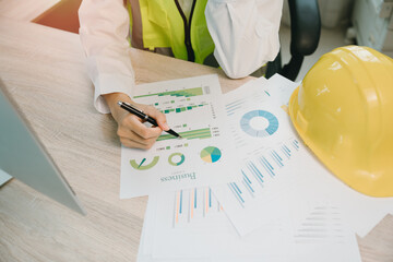 Business analysis with charts and graphs by engineer in safety vest with hard hat working on project data in modern office