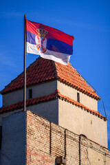 Serbian flag waving atop a historic brick tower under a blue sky