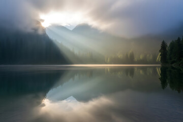 Sun rays breaking through clouds over a misty lake and forest