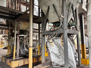 A large industrial silo or hopper in a factory setting, with heavy-duty machinery and equipment. The image captures the complex and raw environment of a working industrial plant, highlighting the proc