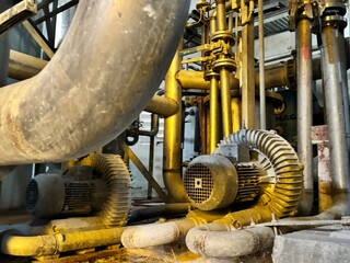 Industrial blower and piping system inside a factory, showing dusty machinery, steel pipelines, and...